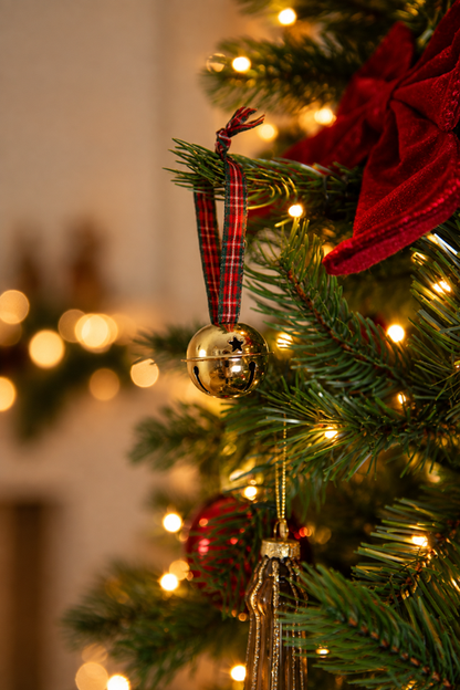 Detail van A Christmas Heritage kerstboomversiering met een gouden kerstbel aan een Schots geruit lint, een rode kerststrik en warme kerstverlichting.
