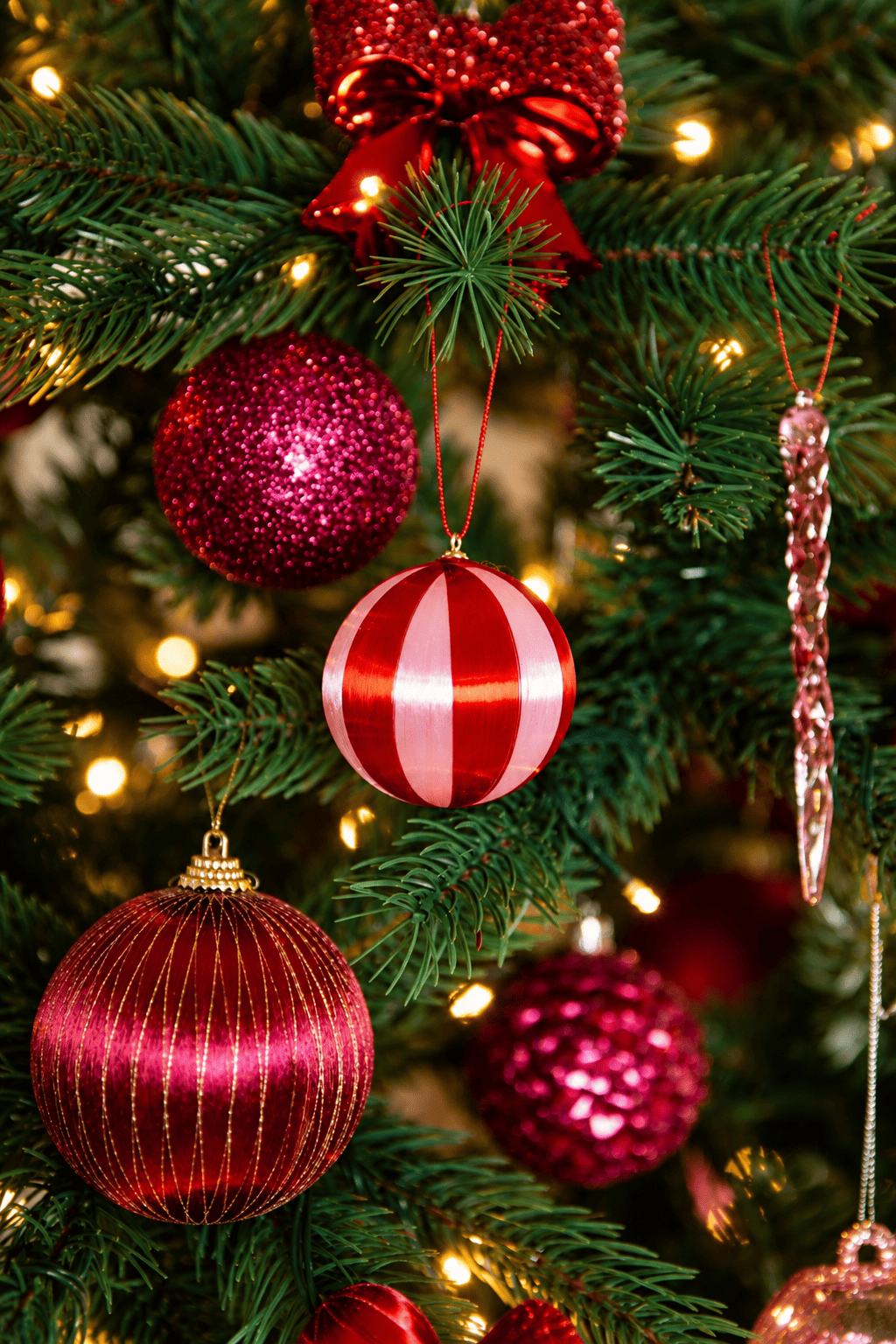 Detail van A Jolly Christmas kerstboomversiering met rode en roze kerstballen, een rood-wit gestreepte kerstbal, roze ijspegelhanger en warme kerstverlichting.