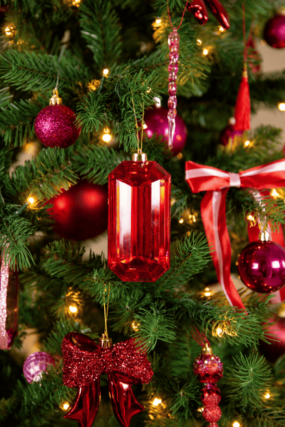 Detail van A Jolly Christmas kerstboomversiering met een langwerpige rode glazen kersthanger, roze en rode kerstballen, feestelijke glitterstrikken en warme kerstverlichting.