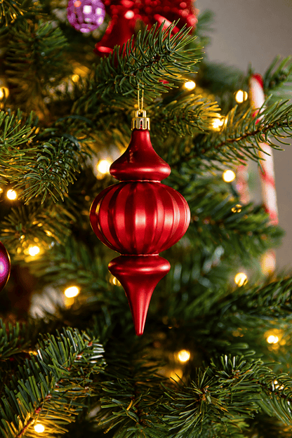 Detail van A Jolly Christmas kerstboomversiering met een langwerpige rode kersthanger met geribbelde kerstbal, omringd door groene dennentakken en warme kerstverlichting.