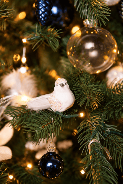 Detail van Snow White Christmas kerstboomversiering met een witte siervogel, transparante en donkerblauwe kerstballen, een blauwe dennenappelhanger en warme kerstverlichting.