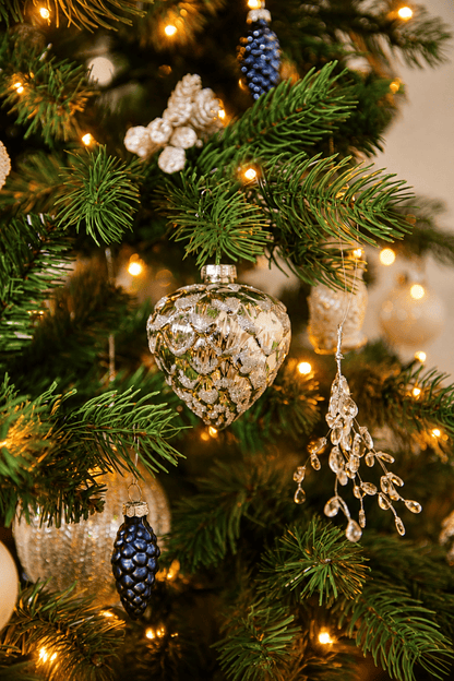 Detail van Snow White Christmas kerstboomversiering met een zilveren dennenappelhanger, blauwe dennenappels, transparante kristalhangers en warme kerstverlichting.