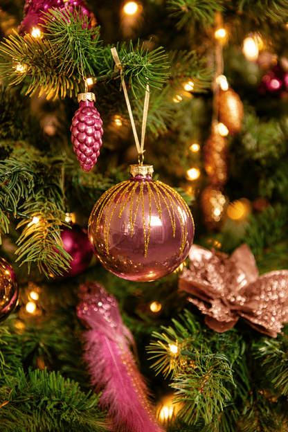 Detail van Warm Christmas Wishes kerstboomversiering met een roze kerstbal met gouden glitters, roze dennenappel, sierveer en warme kerstverlichting.