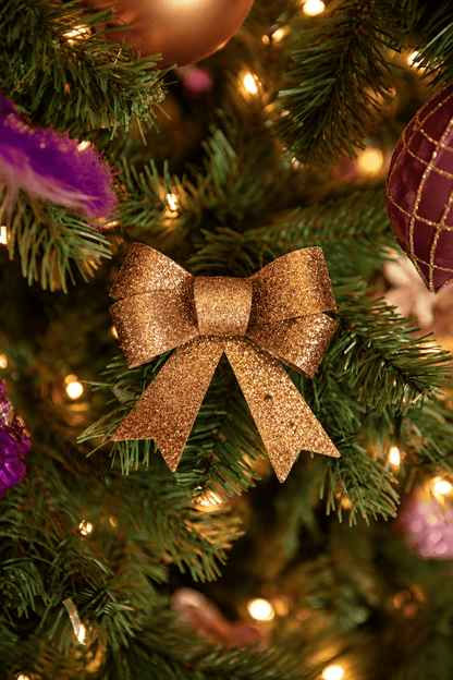 Detail van Warm Christmas Wishes kerstboomversiering met een gouden glitterstrik, paarse sierveer, roze kersthanger en warme kerstverlichting.