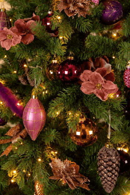 Detail van Warm Christmas Wishes kerstboomversiering met roze en paarse kerstballen, roze kerstbloemen, gouden accenten, een dennenappel en warme kerstverlichting.